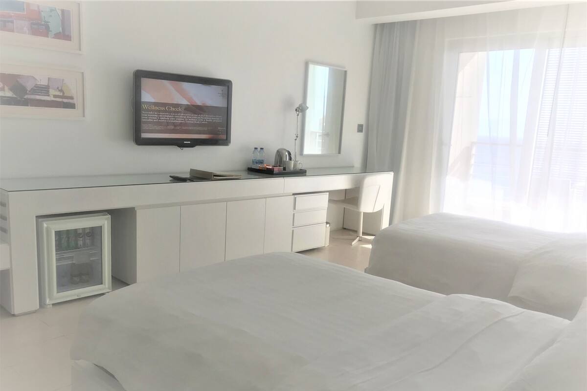 A hotel room with a bed, a desk with a computer, a refrigerator, and a window with curtains.
