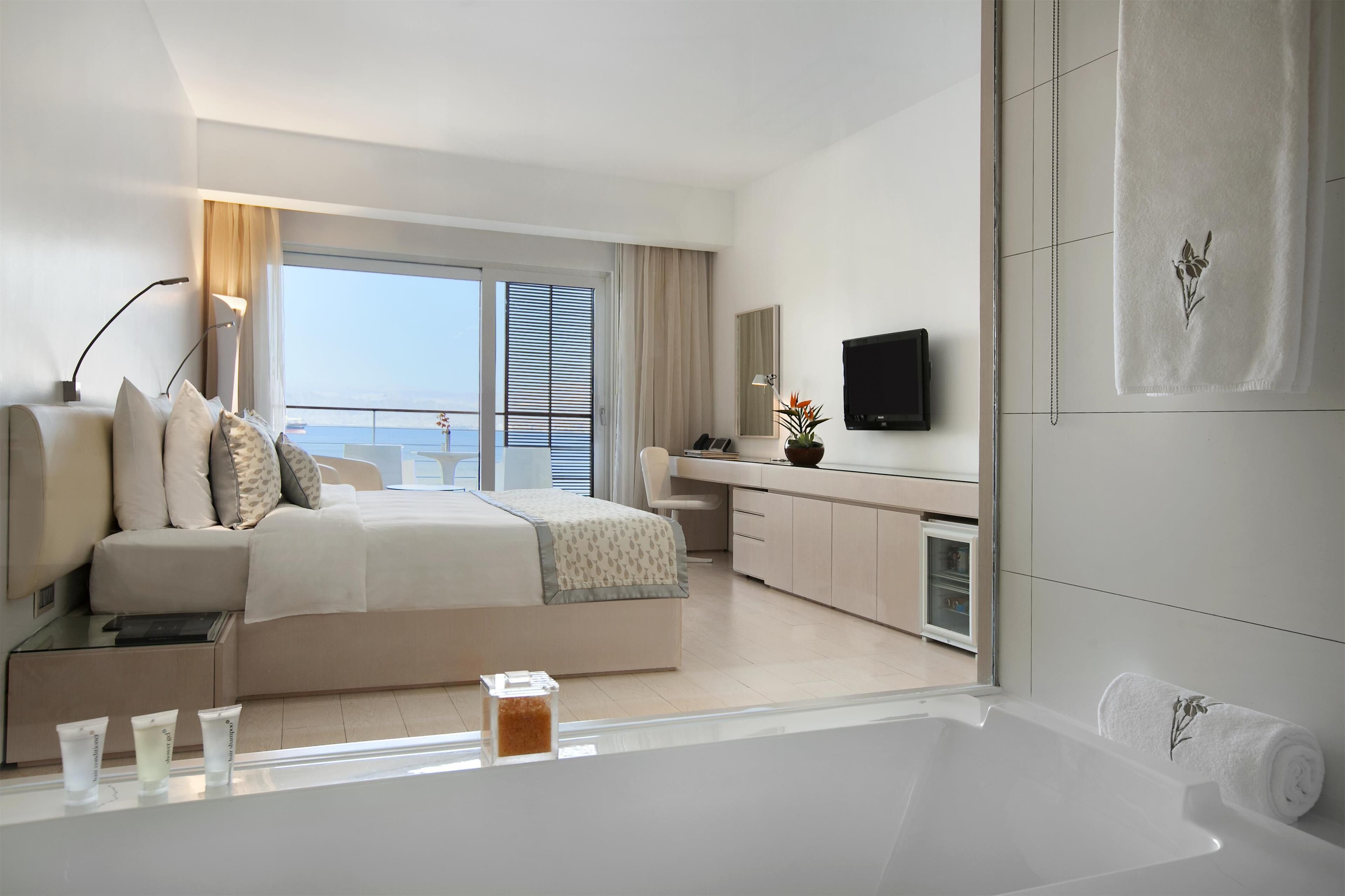 A modern hotel room with a large bed, a desk, a TV, and a bathroom with a bathtub.