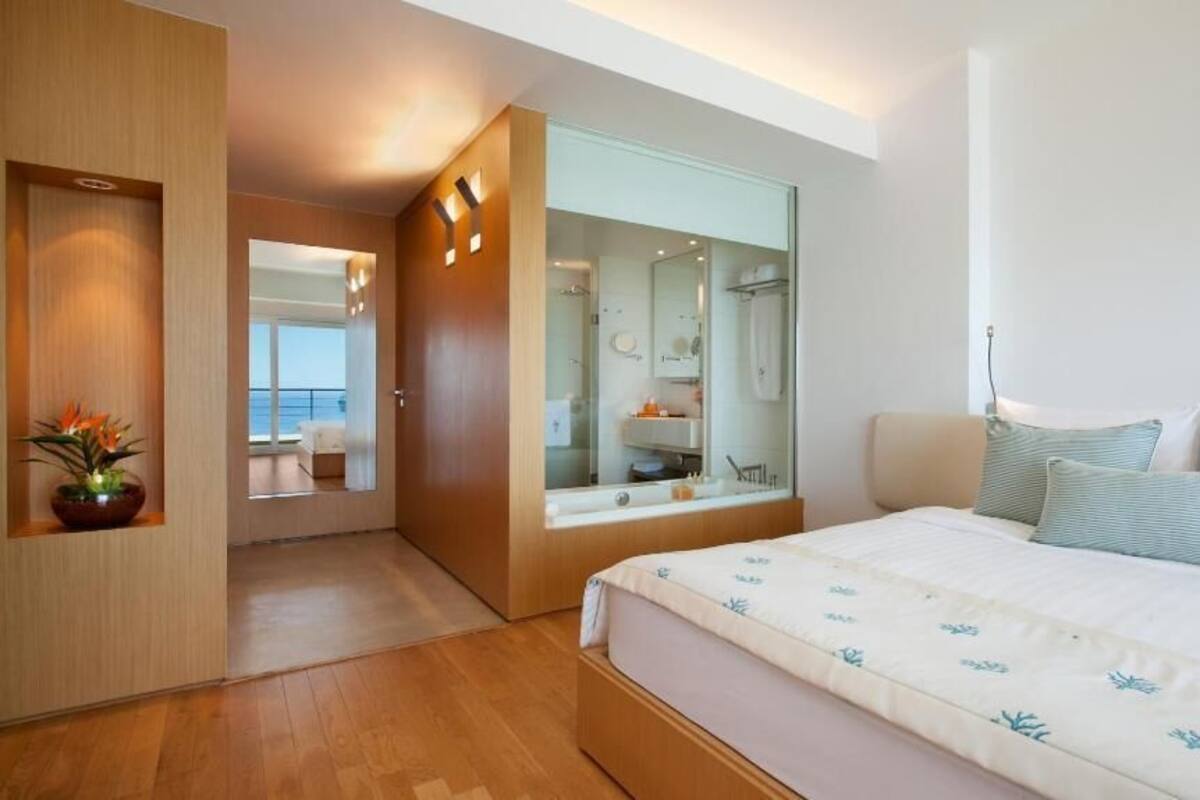A modern bedroom with a large bed, a built-in shower, and a view of the balcony.