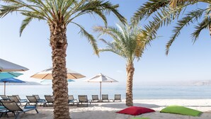 A beach with palm trees, lounge chairs, and umbrellas.