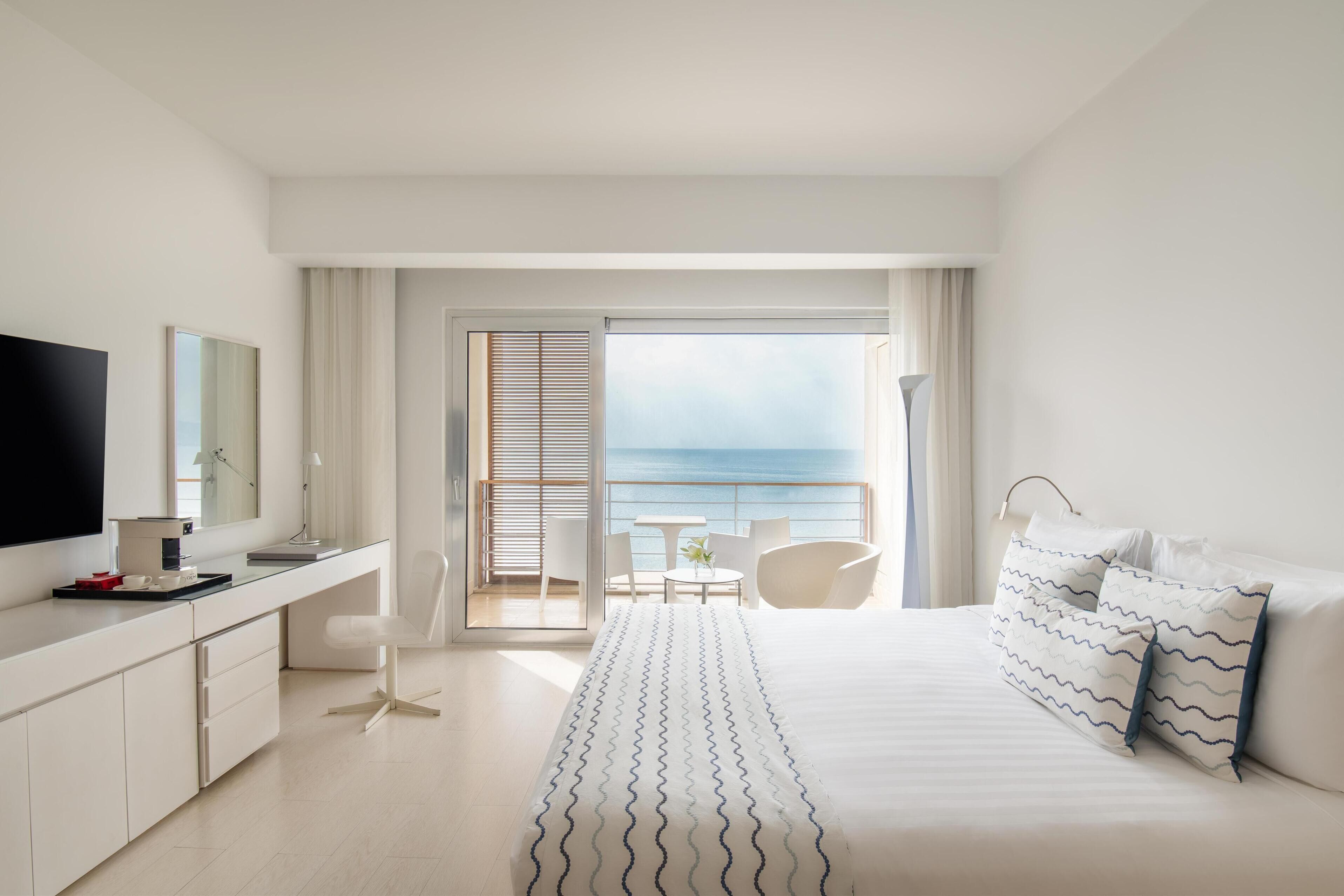 Habitación de hotel moderna con una cama grande, un escritorio, un televisor y un balcón con vistas al mar.