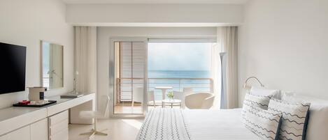 Habitación de hotel moderna con una cama grande, un escritorio, un televisor y un balcón con vistas al mar.
