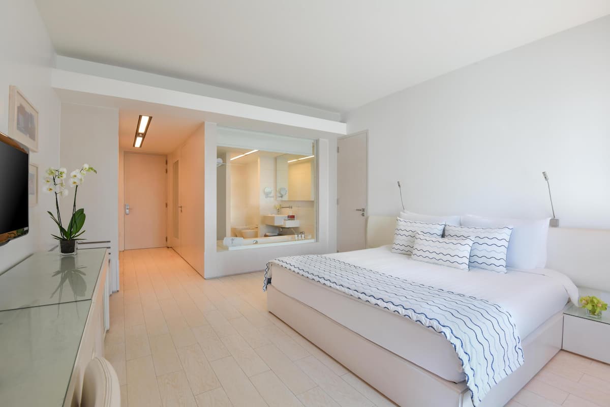 A modern bedroom with a large bed, a glass desk, and a walk-in closet.