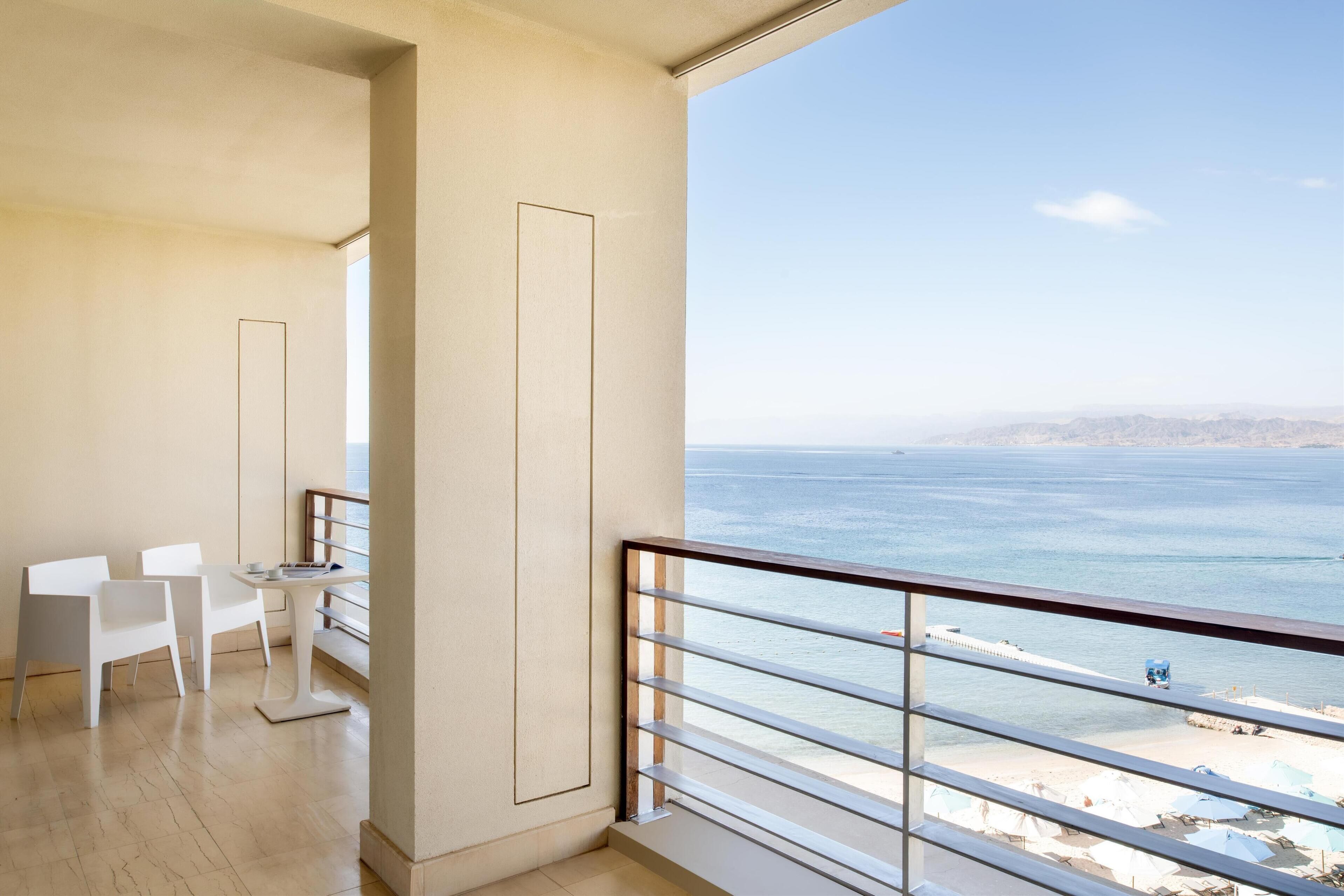 Uma varanda com vista para o mar, uma área de refeições com cadeiras e uma mesa, e uma janela grande.