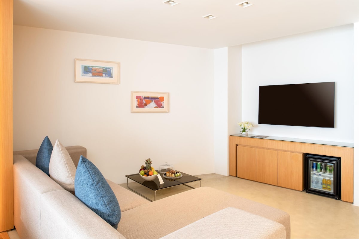 A modern living room with a sofa, coffee table, flat-screen TV, and a mini-fridge.