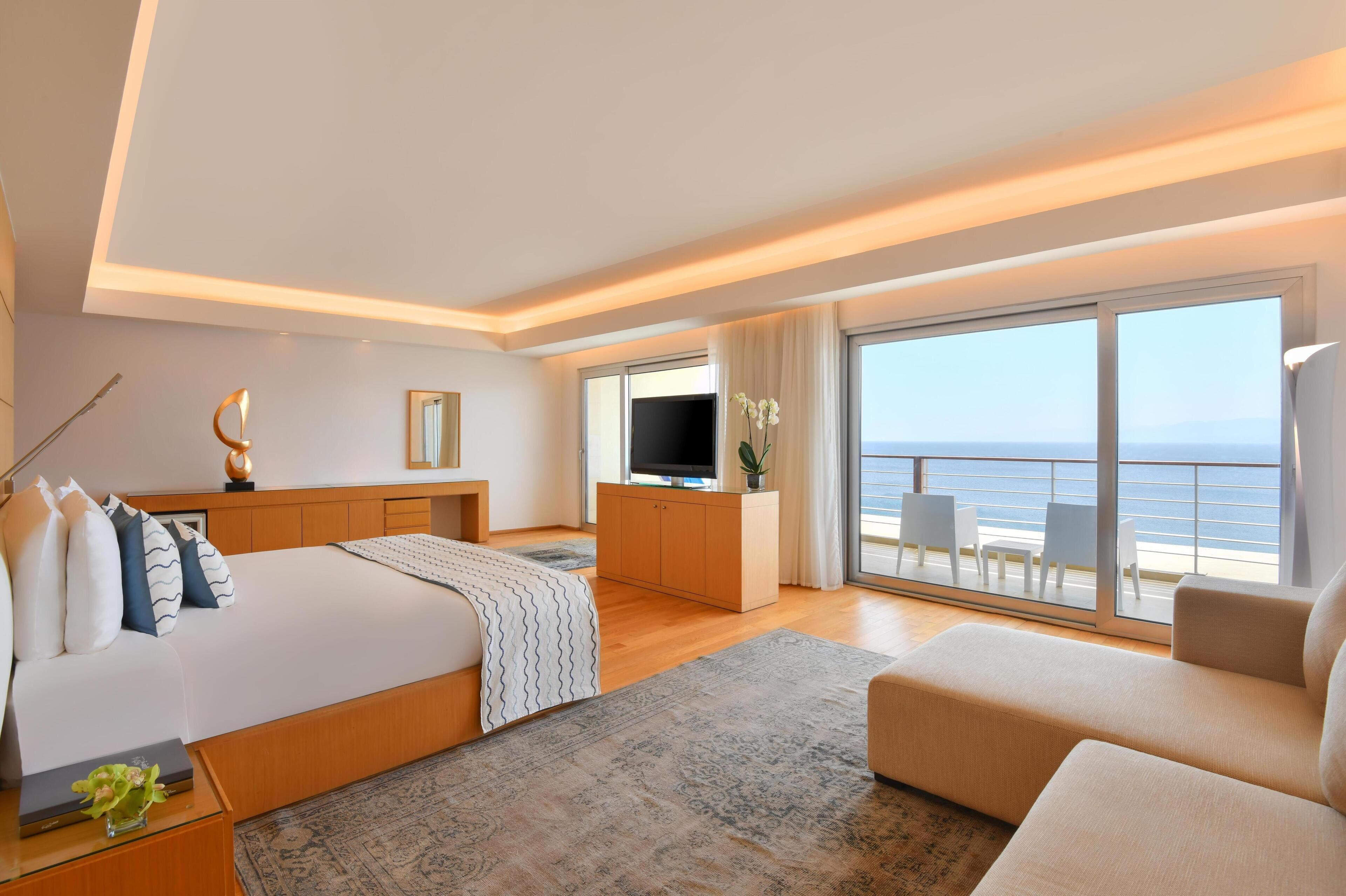 Ett modernt hotellrum med en stor säng, en TV, ett skrivbord och en balkong med utsikt över havet.