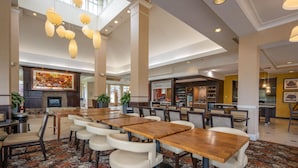 A spacious indoor area with multiple dining tables and chairs, a fireplace, and a large artwork on the wall. - Hilton Garden Inn St. Louis Airport (St. Louis)
