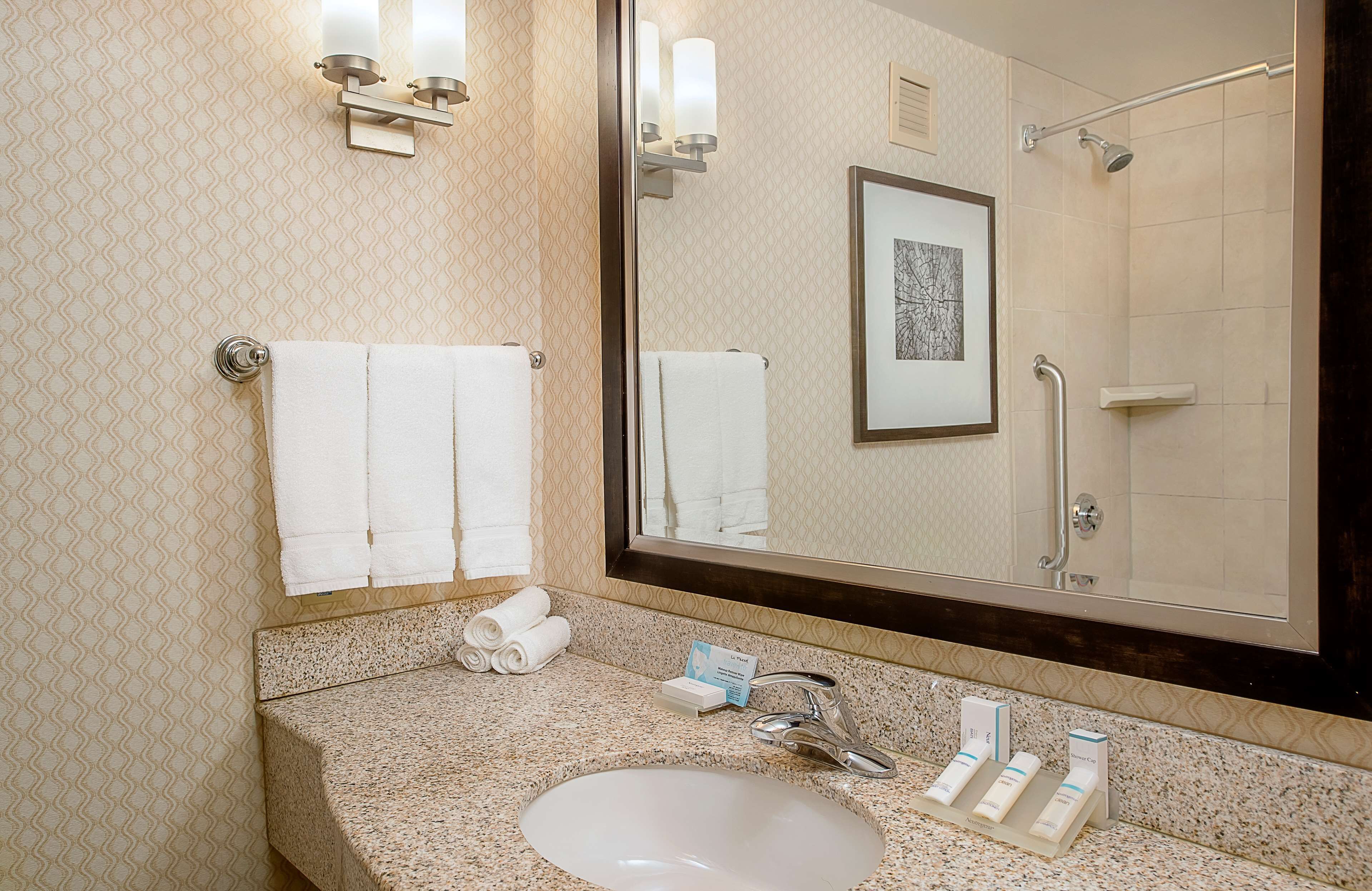 A bathroom with a sink, mirror, towels, and a framed picture on the wall.