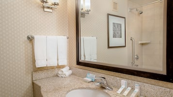 A bathroom with a sink, mirror, towels, and a framed picture on the wall.