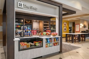 A snack kiosk with a variety of packaged foods and beverages, a cash register, and a sign reading 'The Shop.'