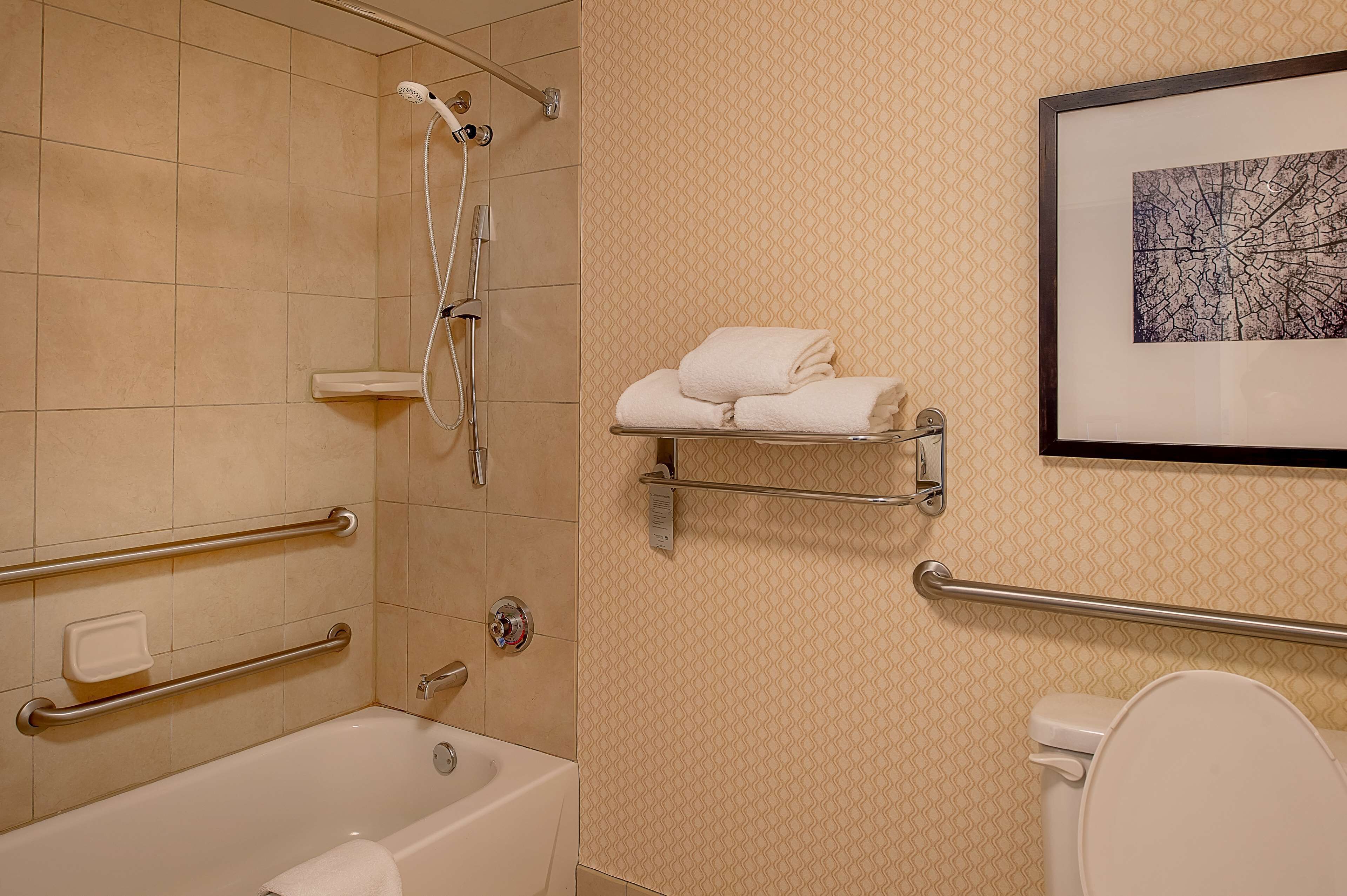 A bathroom with a bathtub, a toilet, and a shower with grab bars. There is a towel rack with folded towels and a framed picture on the wall.