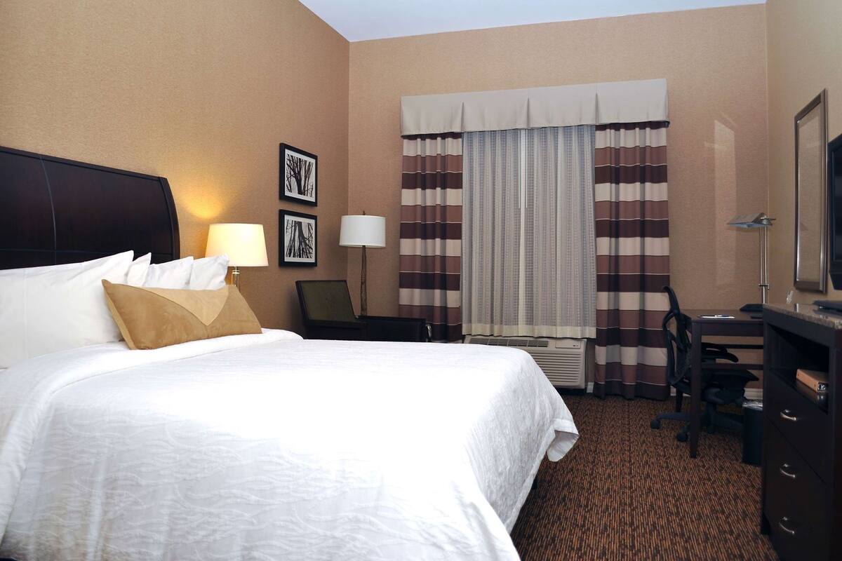 A hotel room with a large bed, a desk, a chair, a lamp, and a television.