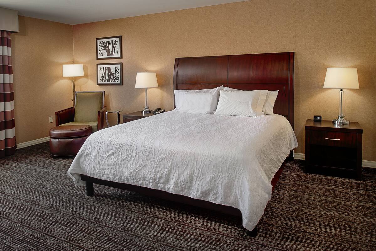 A hotel room with a large bed, two bedside tables with lamps, a chair, and a small table.
