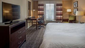 Habitación de hotel con una cama grande, un escritorio con silla, televisor y lámpara.