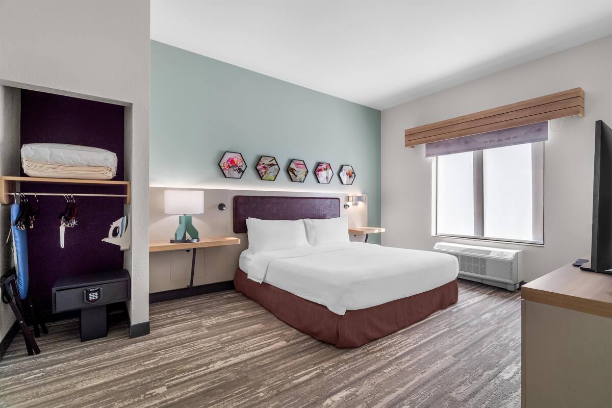 A hotel room with a bed, a desk, a chair, a wardrobe, and a window.