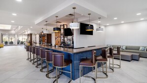 A modern bar area with a long counter, multiple stools, and pendant lighting. - Hilton Garden Inn Cartersville (Cartersville)