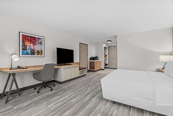 A hotel room with a bed, a desk with a computer and a chair, a television, and a coffee machine.