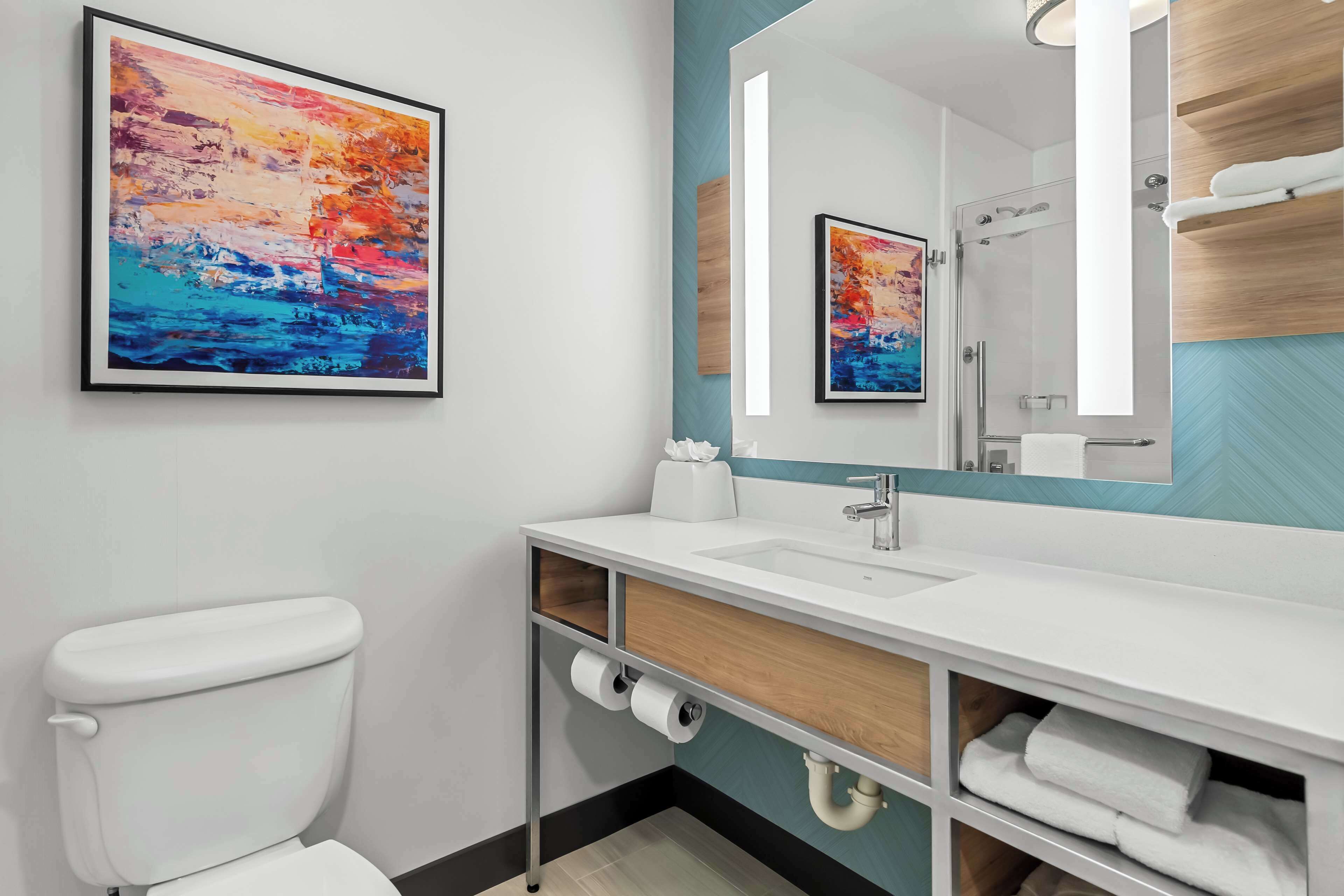 Un baño moderno con inodoro blanco, un espejo grande y un lavabo.
