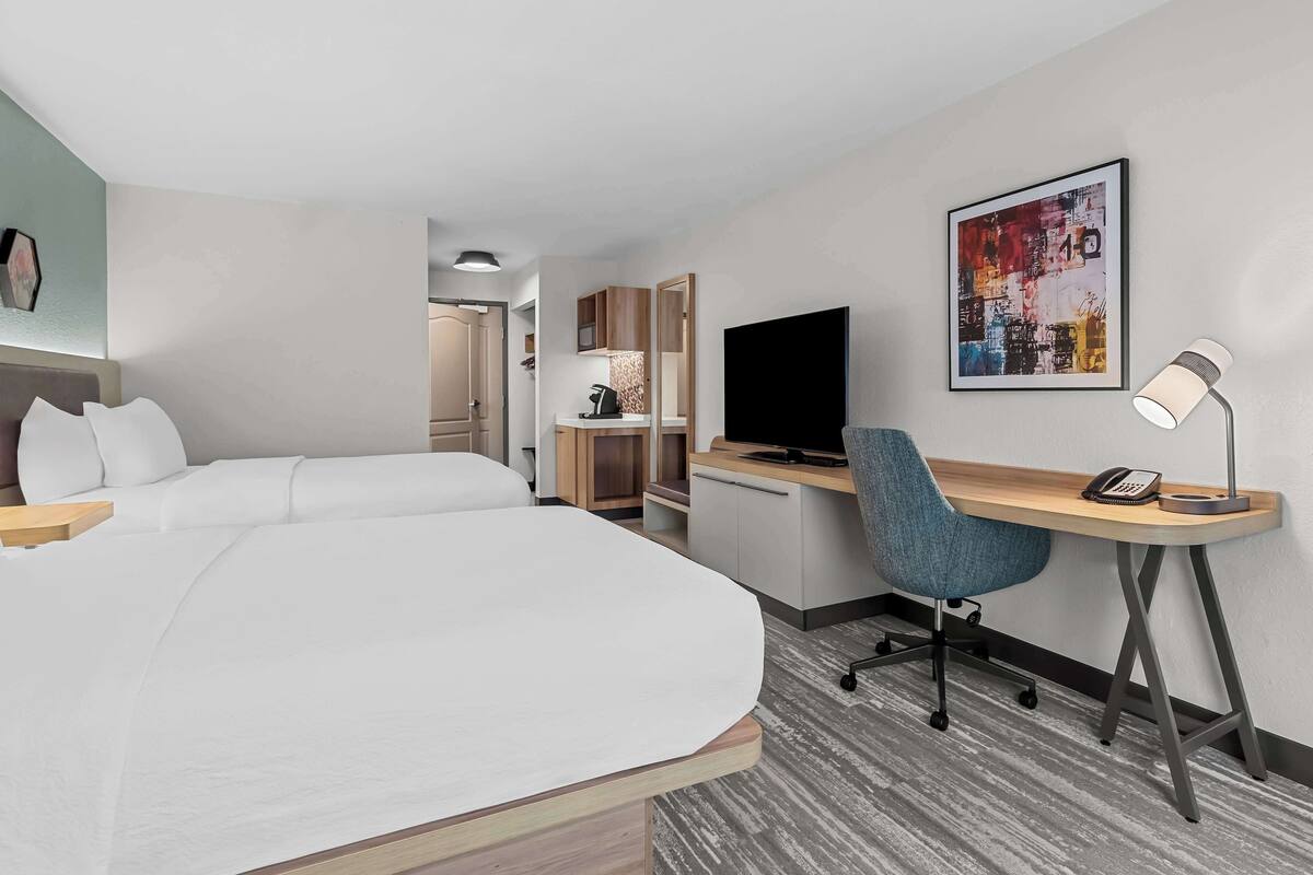 A hotel room with a large bed, a desk with a computer and phone, a chair, a TV, and a painting on the wall.