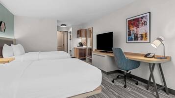 Une chambre d’hôtel avec un grand lit, un bureau équipé d’un ordinateur et d’un téléphone, une chaise, une télévision et un tableau au mur.