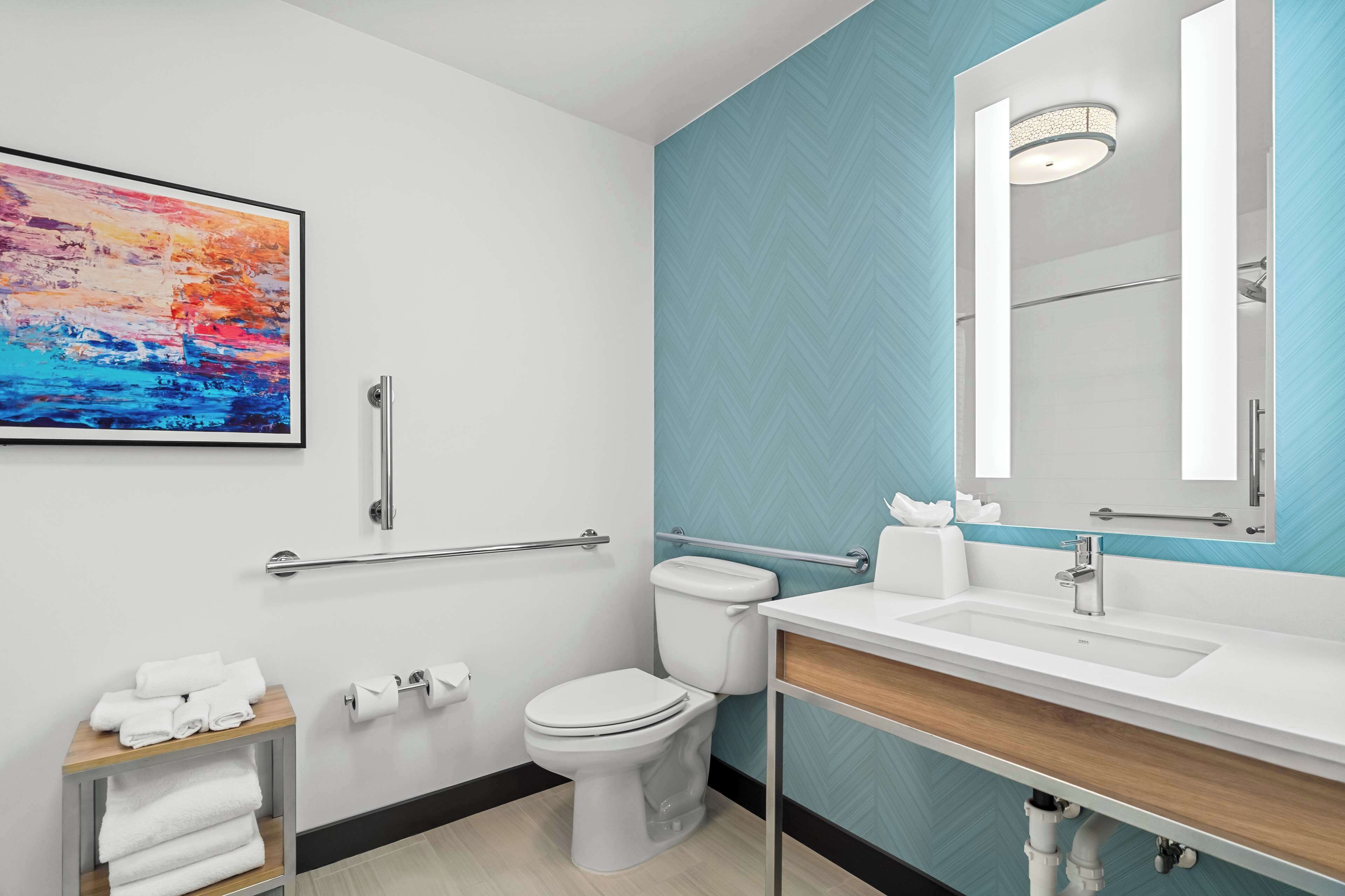 Un baño moderno con inodoro blanco, lavabo con espejo y un perchero para toallas.