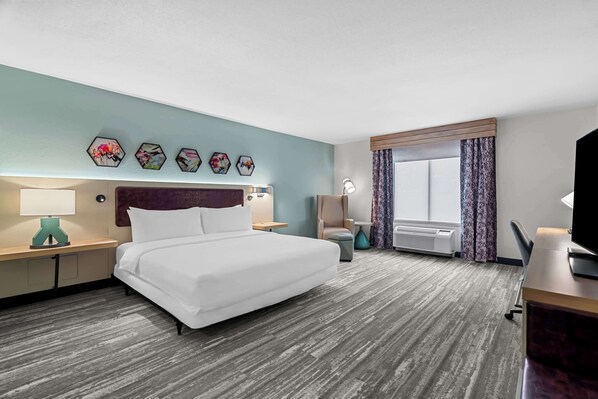 Una habitación de hotel con una cama grande, un escritorio con computadora, una silla, una ventana con cortinas y un televisor montado en la pared.