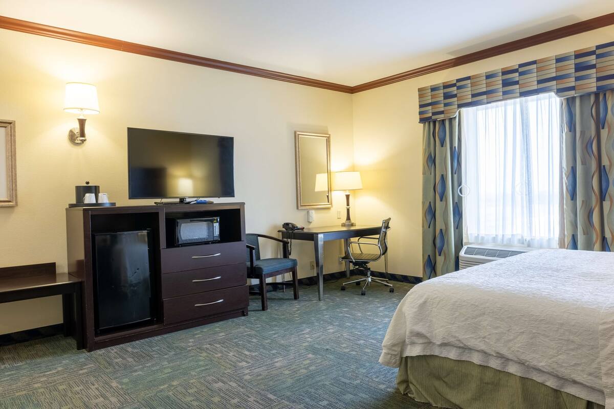 Une chambre d’hôtel équipée d’un lit, d’un bureau, d’une chaise, d’une télévision et d’un petit réfrigérateur.