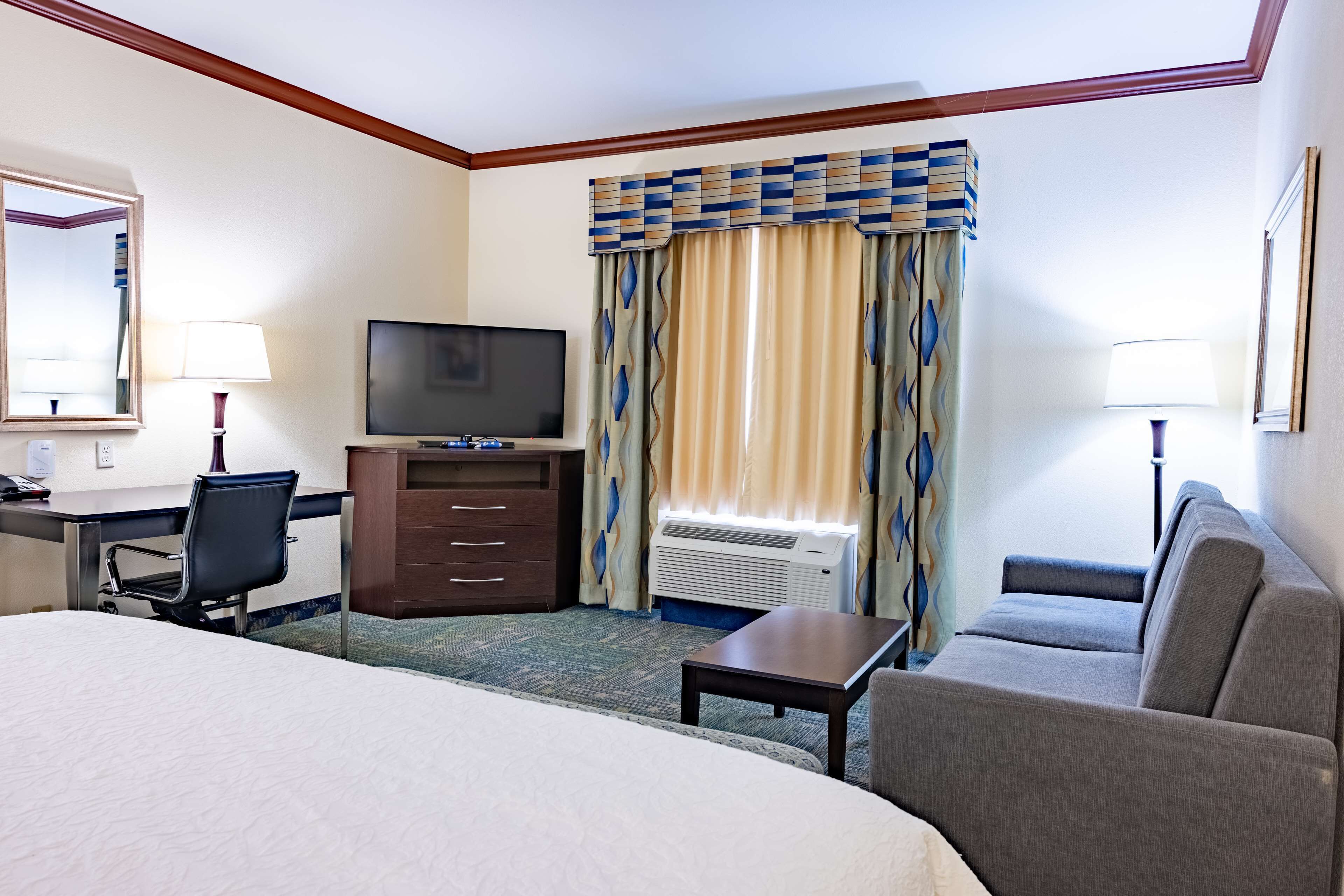 Habitación de hotel con cama, escritorio con silla, televisión, sofá y ventana con cortinas.