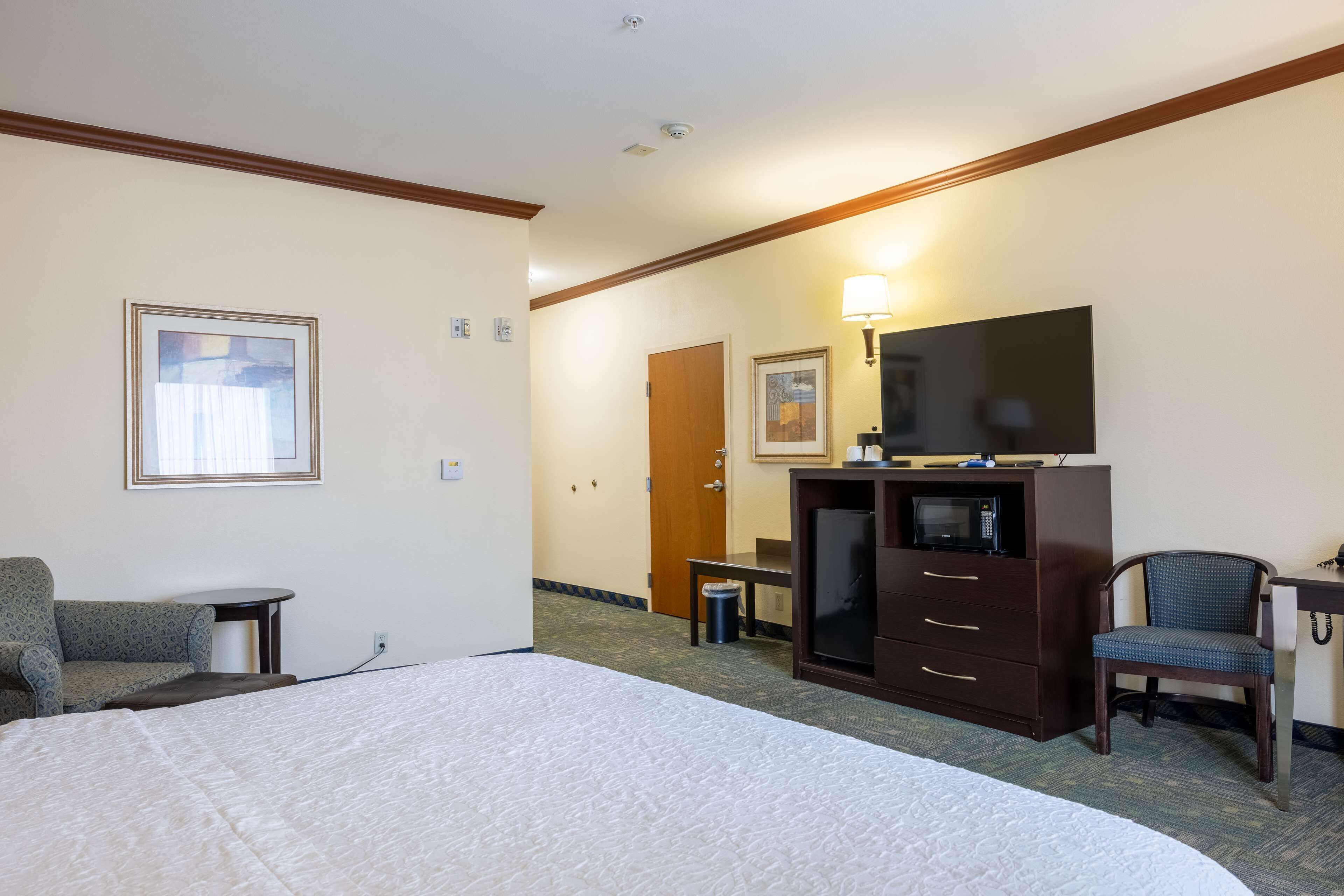 A hotel room with a large bed, a desk with a chair, a television, and a microwave.