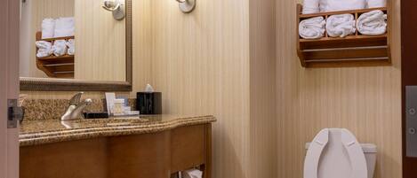 A bathroom with a wooden vanity, a large mirror, a toilet, and a shelf with towels.