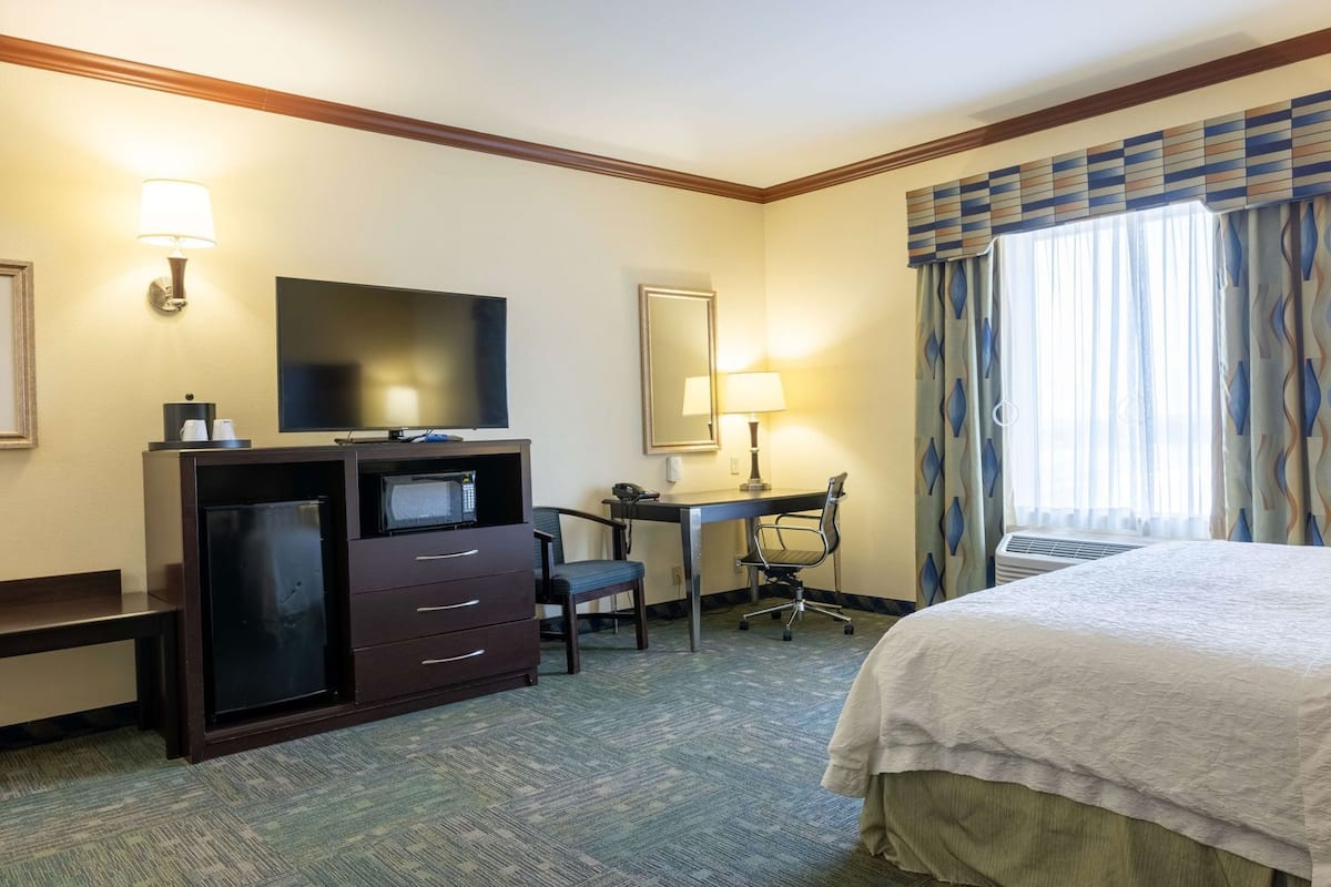 Ein Hotelzimmer mit Bett, Schreibtisch mit Stuhl, Fernseher, Mikrowelle und Lampe.