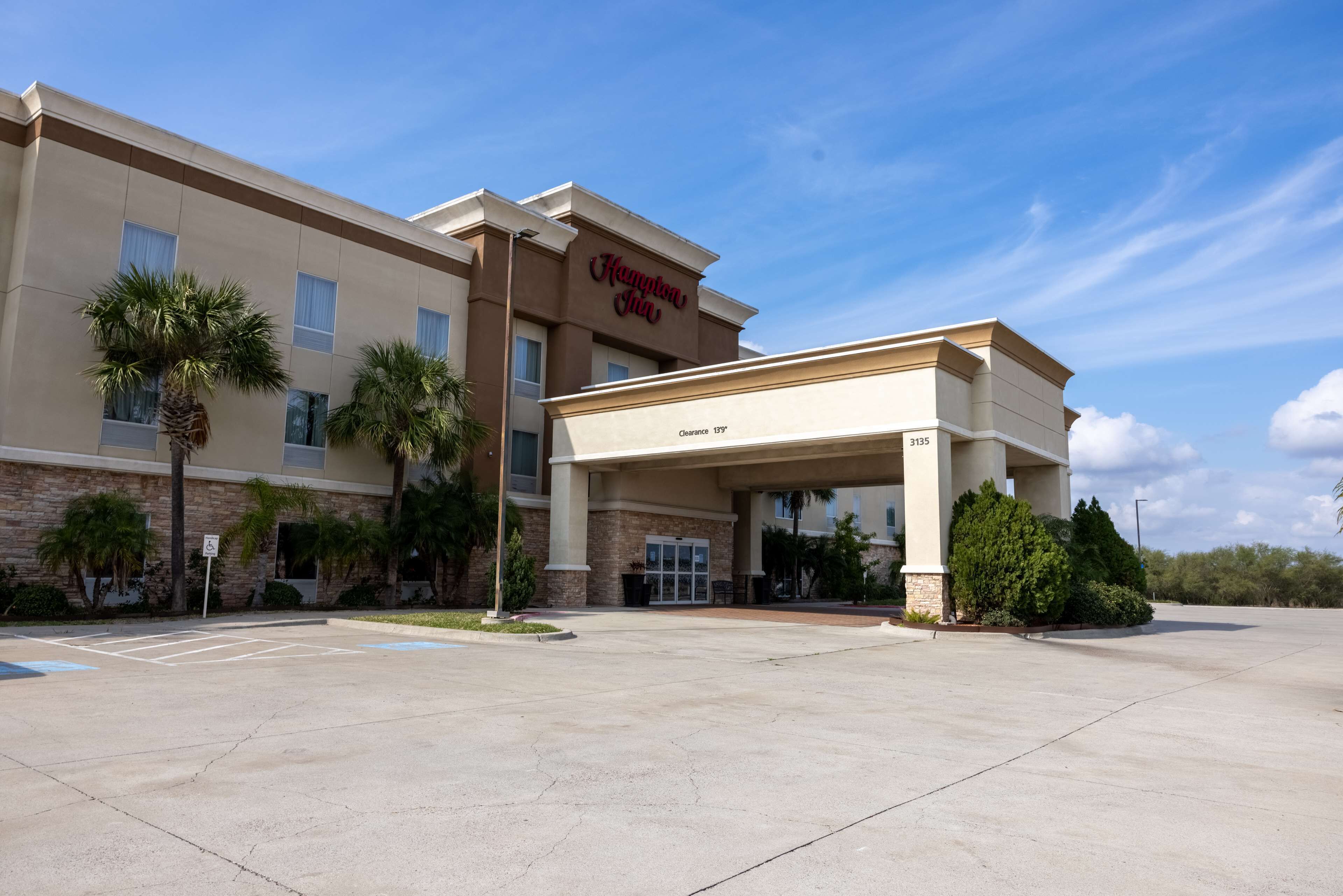 Un hôtel Hampton Inn doté d’une entrée abritée, d’un parking et de palmiers.