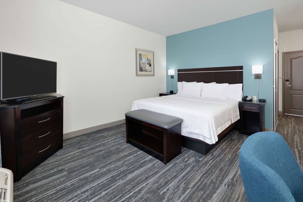 A hotel room with a bed, bedside tables, a TV, a bench, and a chair.