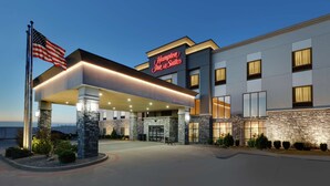Een modern hotel met een gevel van natuursteen, een opvallend 'Hampton Inn & Suites' bord en een Amerikaanse vlag.