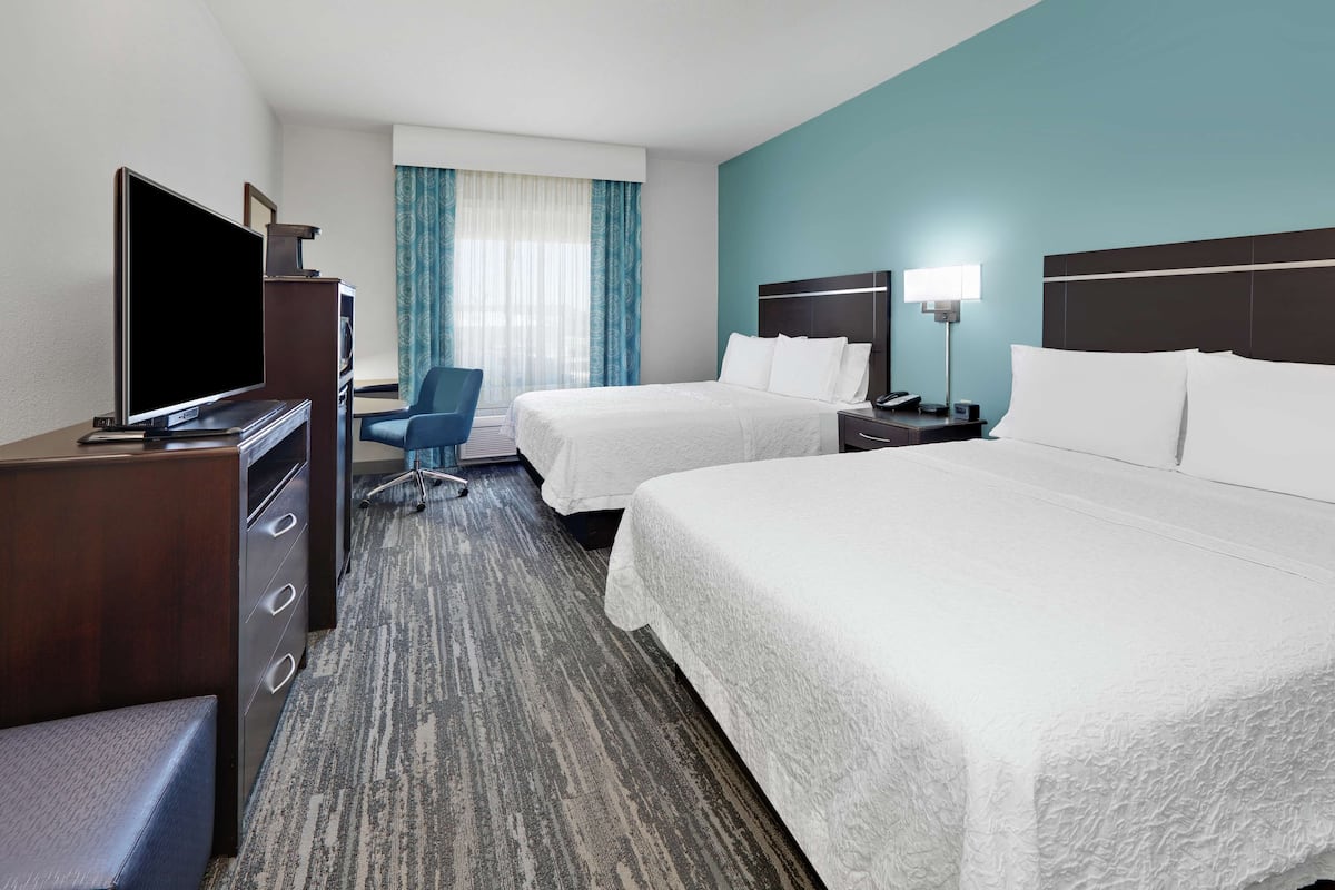 A hotel room with two beds, a desk with a TV, a chair, and a window with curtains.