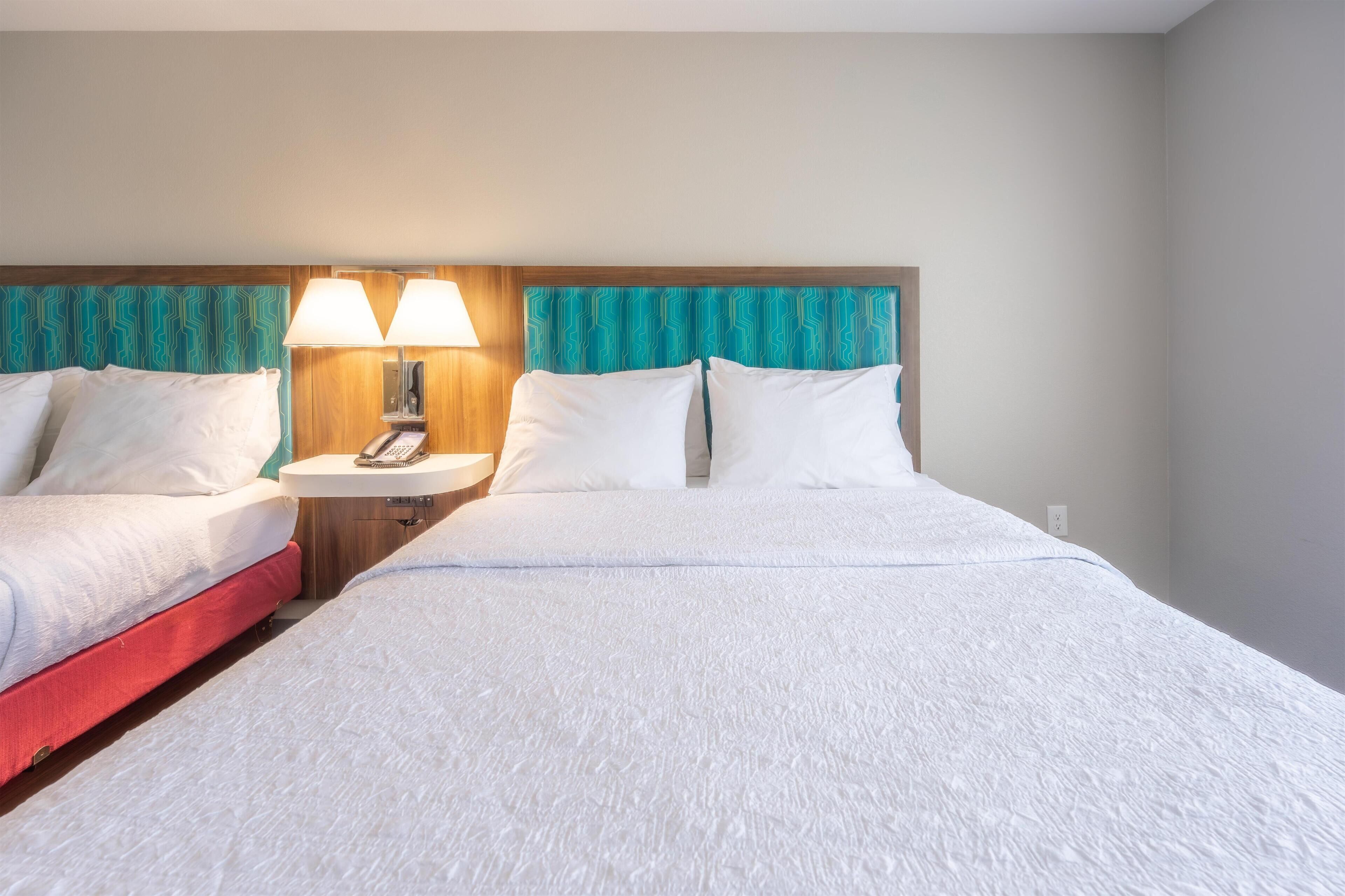 Une chambre d’hôtel avec deux lits, une table de chevet avec une lampe et une tête de lit en bois.