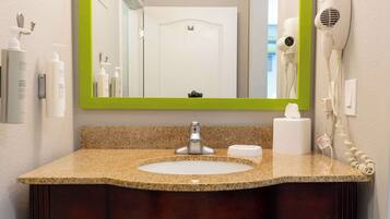 A bathroom with a granite countertop, a white sink, a mirror with a green frame, and a hair dryer mounted on the wall.