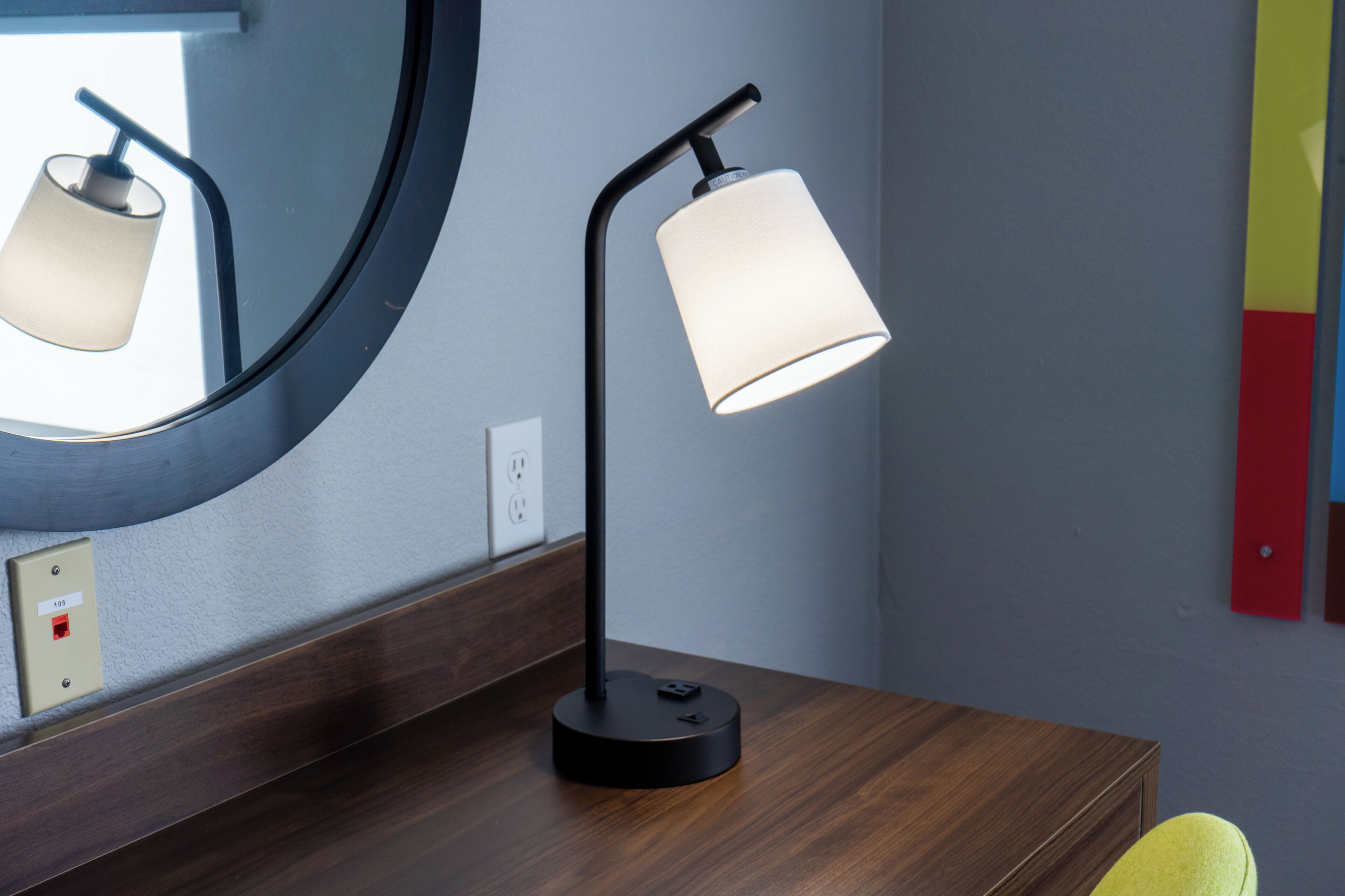 Una lámpara de escritorio moderna con pantalla cilíndrica, un espejo redondo encima y una superficie de madera.