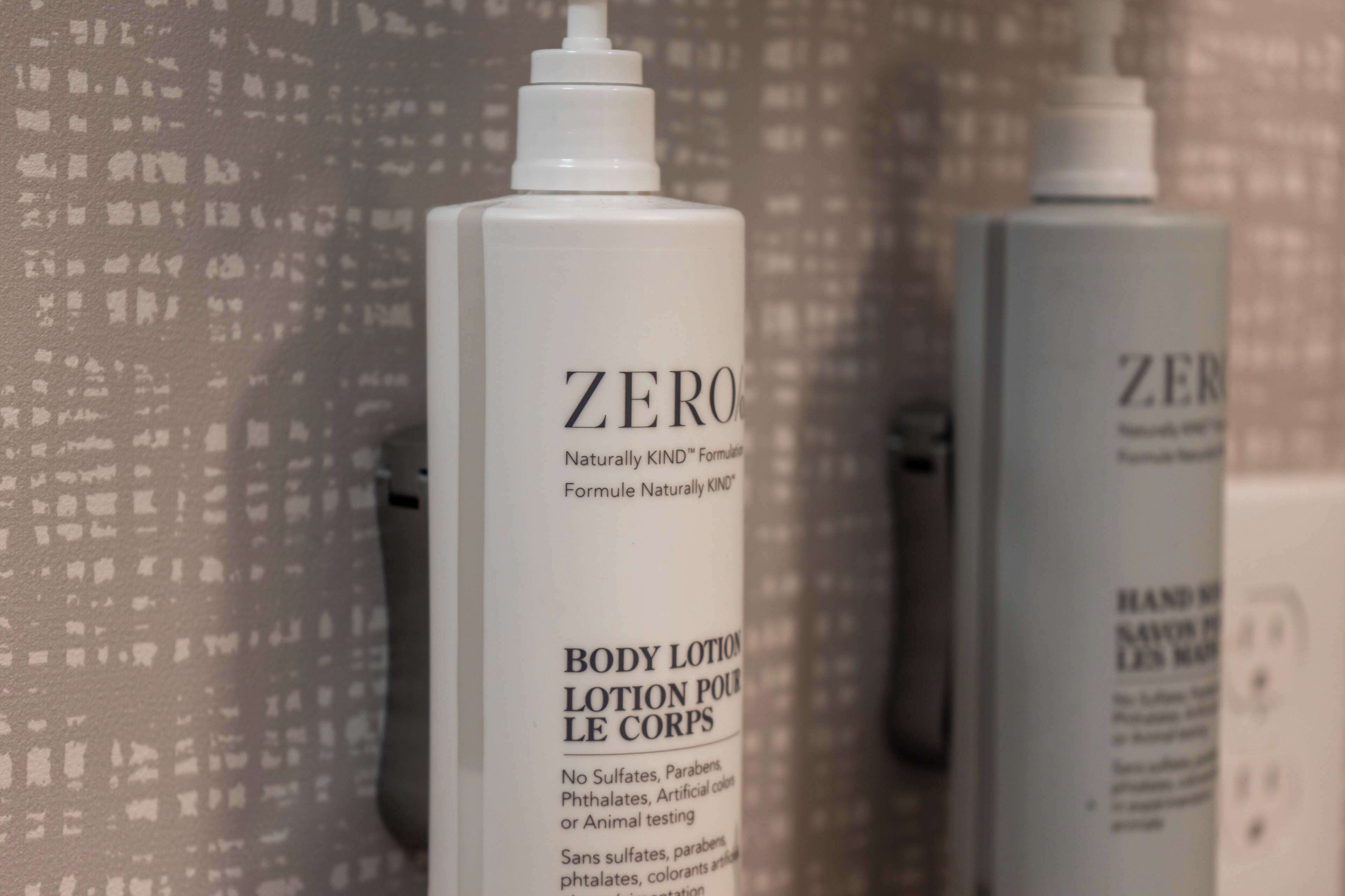Two bottles of Zero body lotion against a patterned wall.