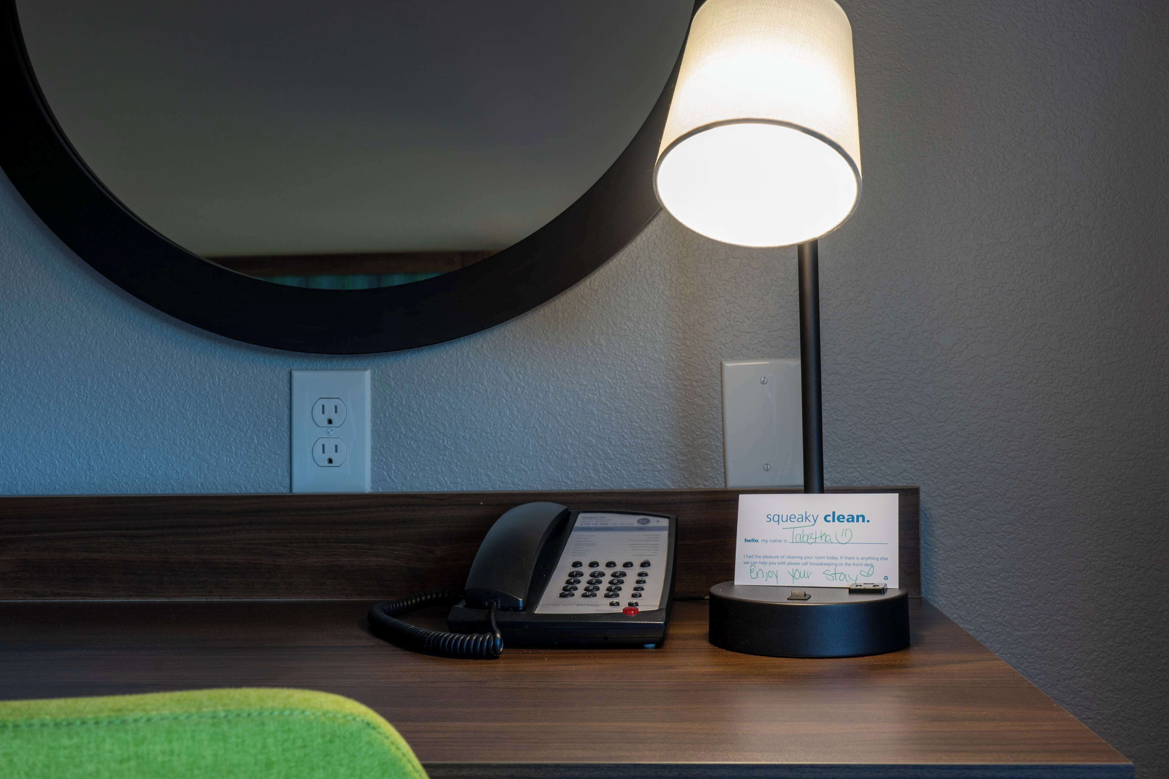 A hotel reception area with a desk, a telephone, a lamp, and a sign indicating the room is clean.