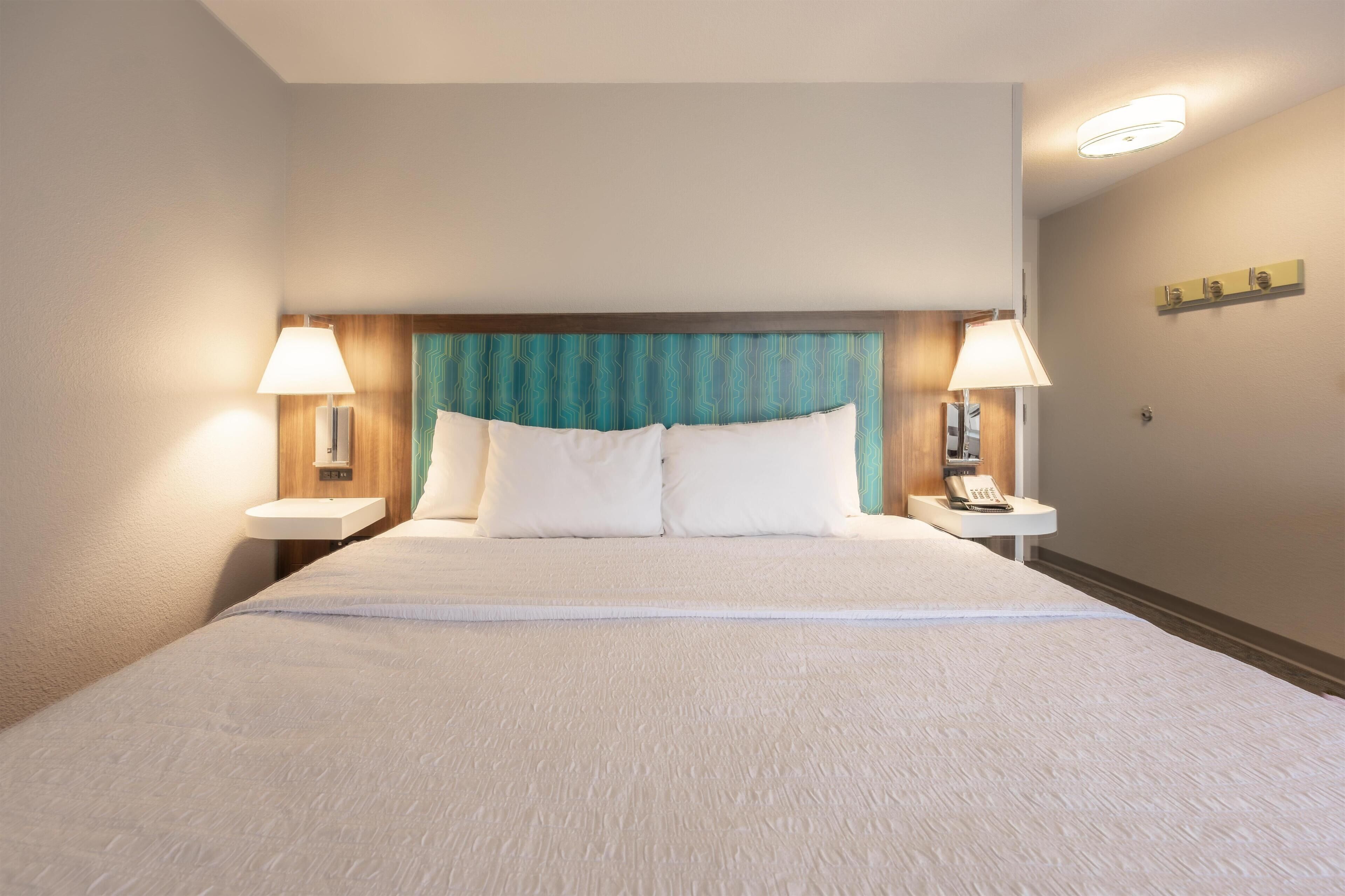 A hotel room with a large bed, two bedside tables with lamps, a wooden headboard, and a small shelf with a telephone.