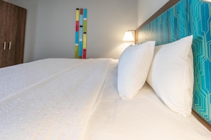 A bed with white bedding, a wooden wardrobe, and a colorful wall decoration. - Hampton Inn Elkhorn Lake Geneva Area (Elkhorn)