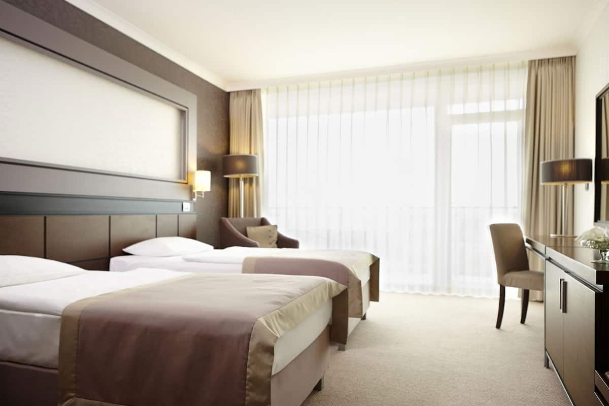 A hotel room with two beds, a desk, a chair, and a large window with curtains.