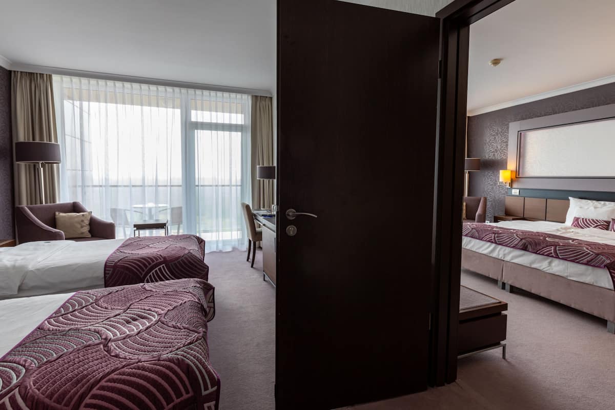 A hotel room with two beds, a desk, a chair, and a large window with curtains.