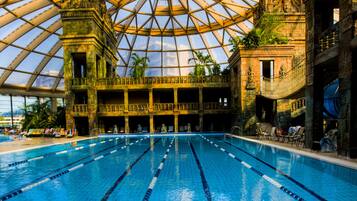 An indoor swimming pool with clear lane markings, a large glass dome ceiling, and a stone building structure in the background.