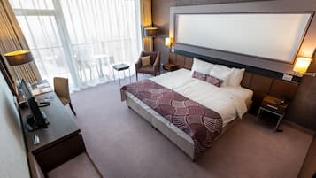 Una habitación de hotel con una cama grande, un escritorio con computadora, una silla, una mesita y una ventana con cortinas.