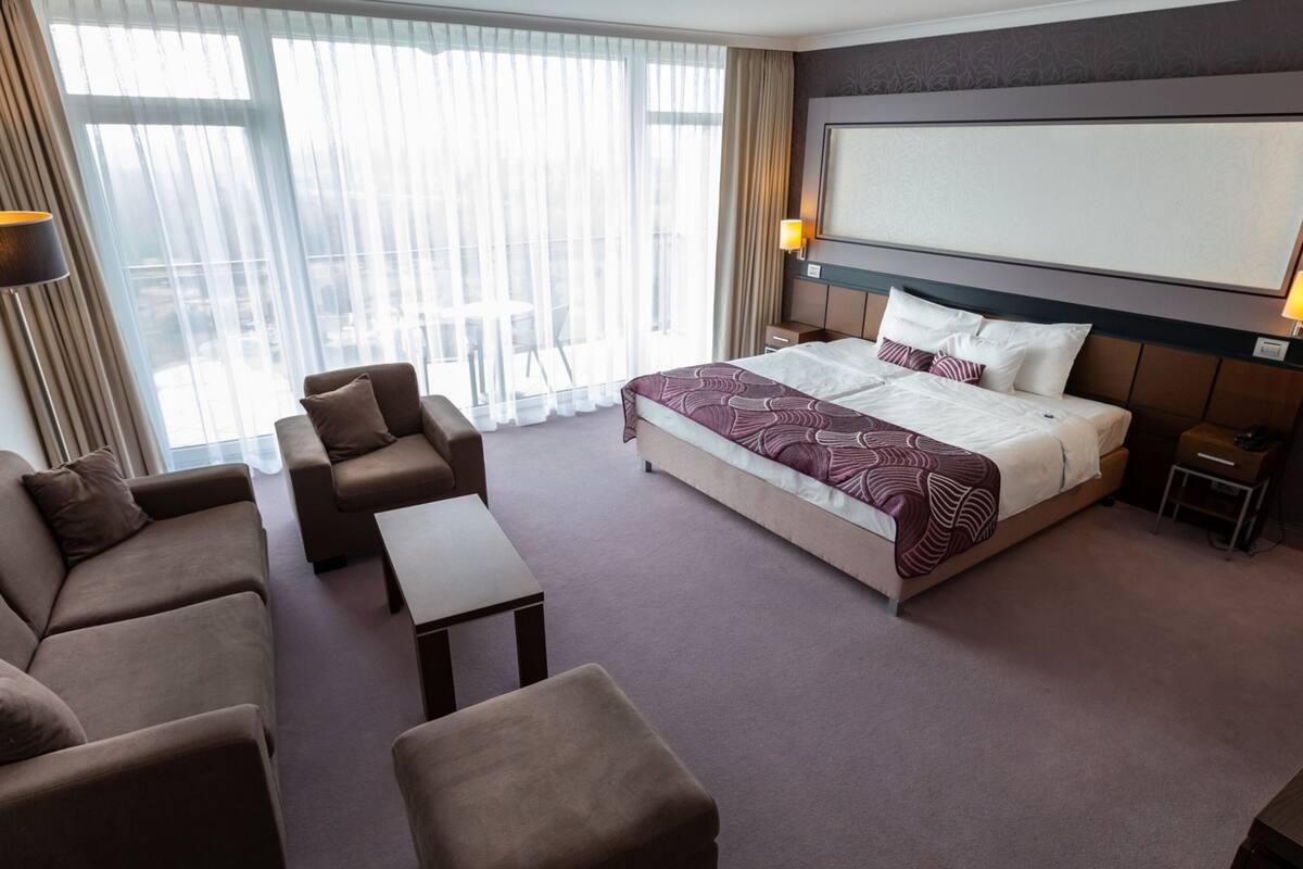 A hotel room with a large bed, a sofa, a chair, a small table, and a TV.