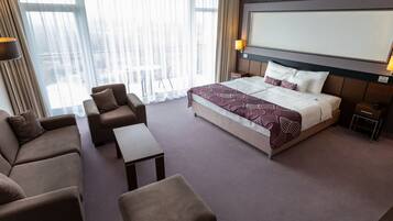 Habitación de hotel con una cama grande, un sofá, una silla, una mesita y un televisor.