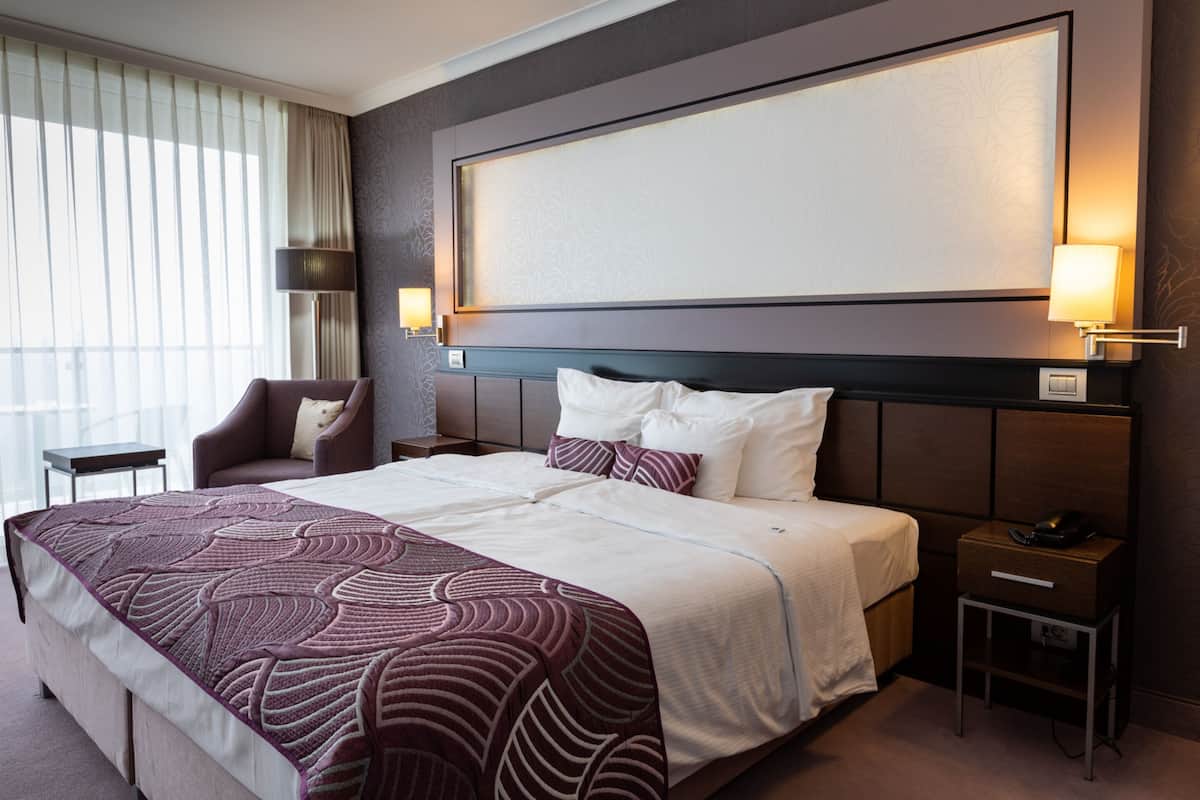 A hotel room with a large bed, a nightstand, a chair, and a window with curtains.