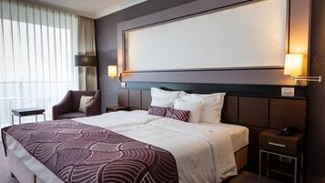A hotel room with a large bed, a nightstand, a chair, and a window with curtains.
